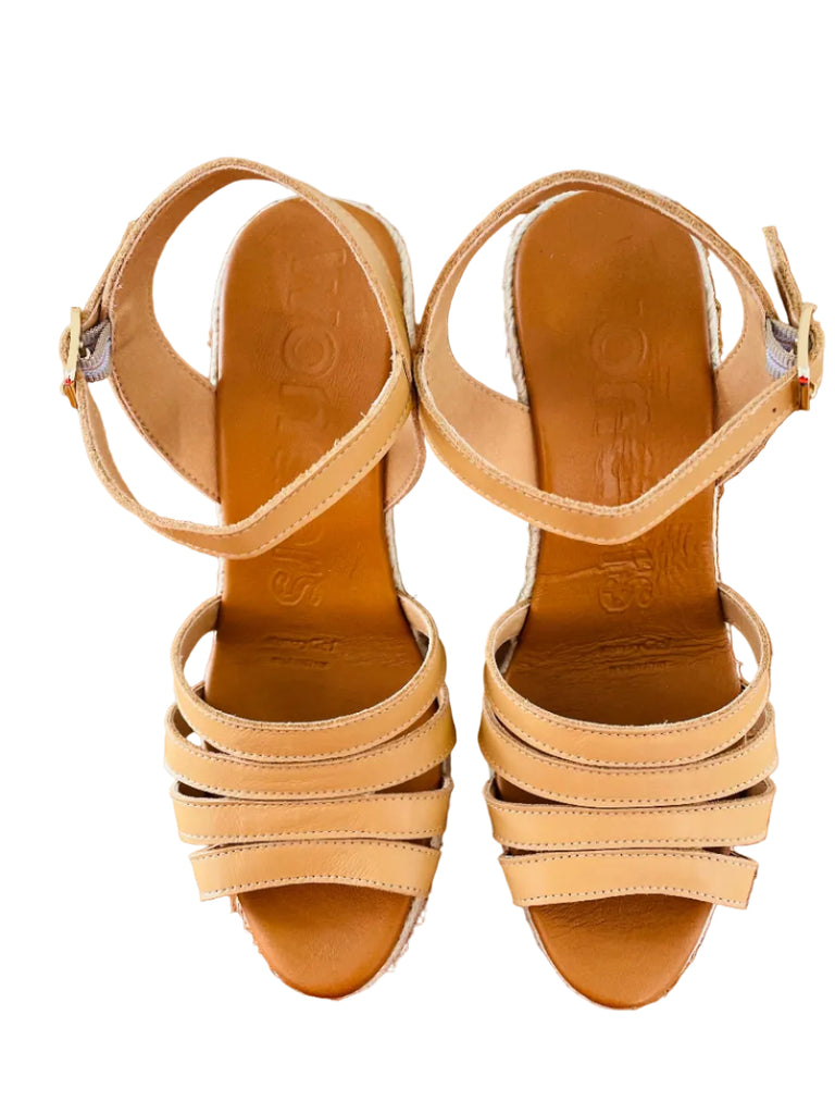 Pair of beige sandals on a wooden surface with a tiled wall in the background