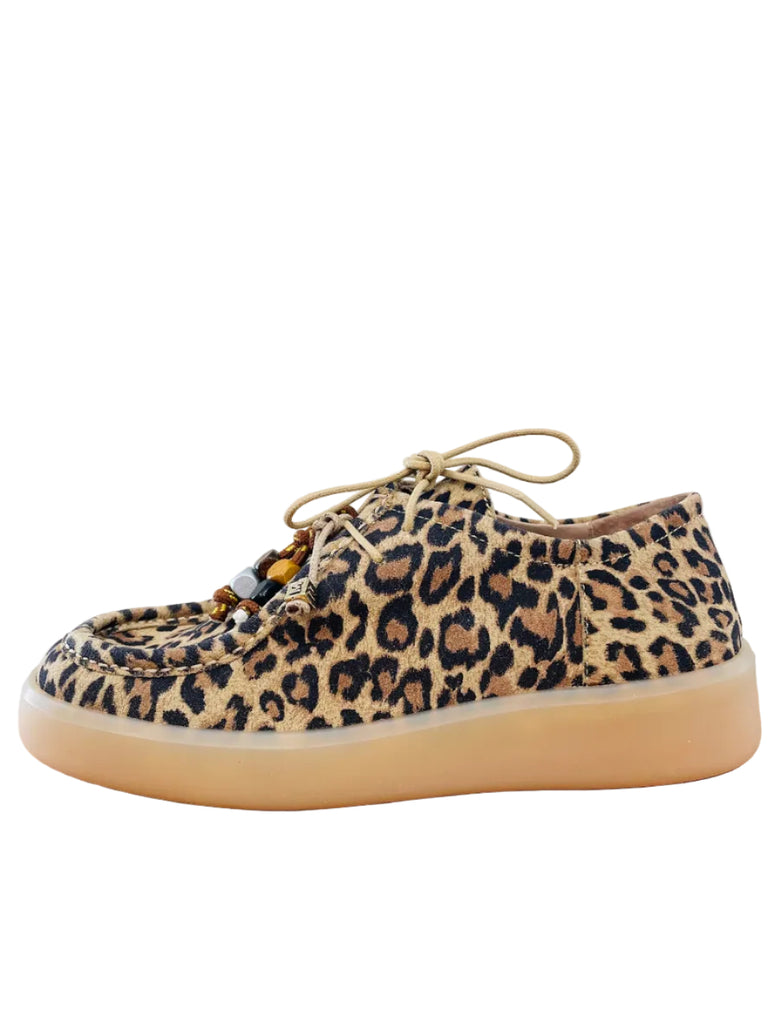 Leopard print sneaker on a wooden surface with a white wall background