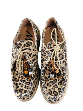 Load image into Gallery viewer, Leopard print sneakers with decorative laces on a wooden surface.
