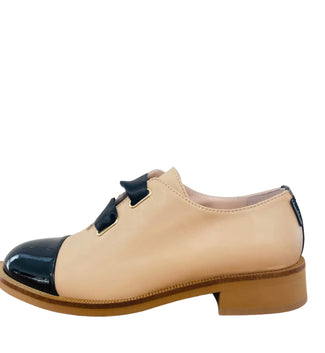 Beige and black shoe on a wooden surface with a white background