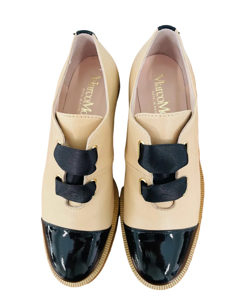 Pair of beige shoes with black patent leather caps on a wooden surface.