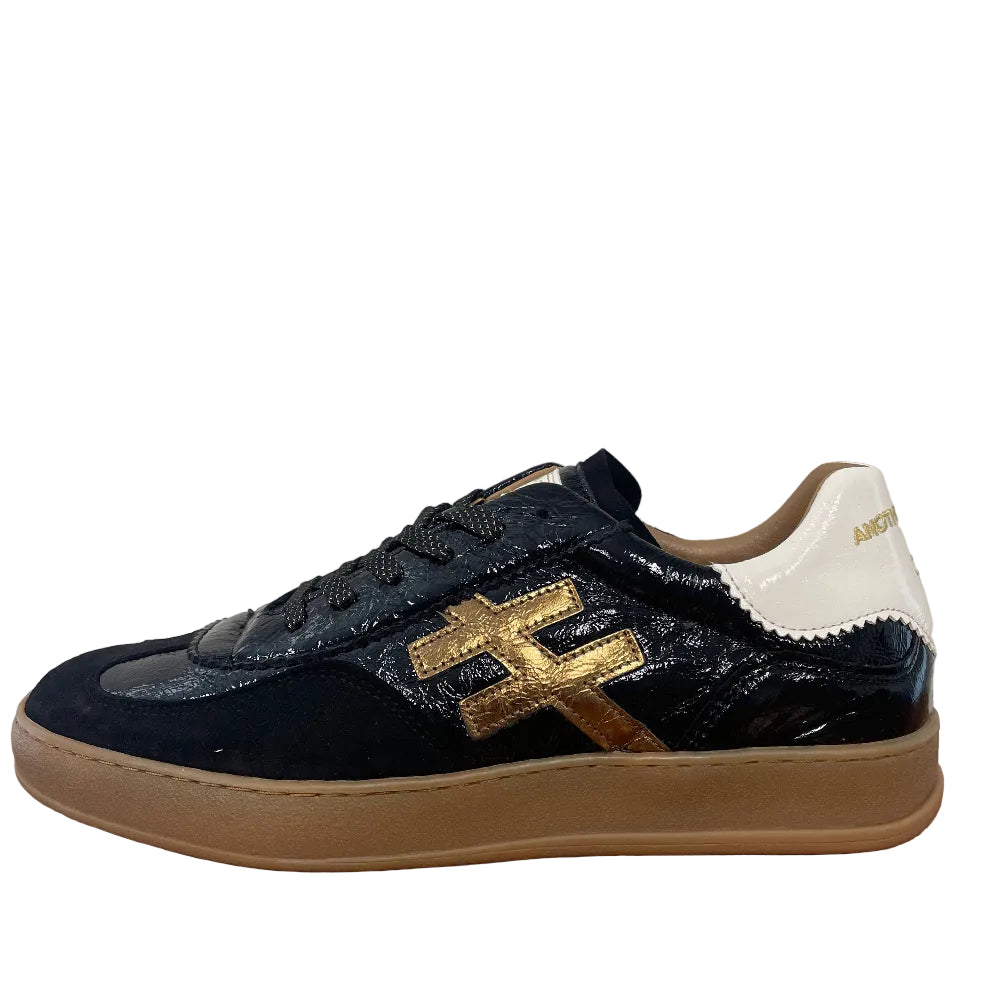 A single black leather sneaker with a prominent gold 'H' logo on the side, a white heel tab, and a beige gum sole, shown standing on a wooden floor against a plain wall.