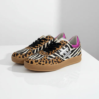 A pair of MOTHER & DOLL low-top sneakers featuring a mixed animal print design with leopard print, zebra print, and black suede, accented with a metallic silver 'X' logo and a bright pink collar, on a white background.