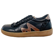 Load image into Gallery viewer, A black leather sneaker with a textured metallic rose gold 'M' logo on the side, black laces, and a thick tan rubber sole, resting on a wooden table against a plain wall.
