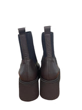Load image into Gallery viewer, A pair of dark brown leather Chelsea boots with platform heels, shown from the back on a wooden tabletop against a plain wall.
