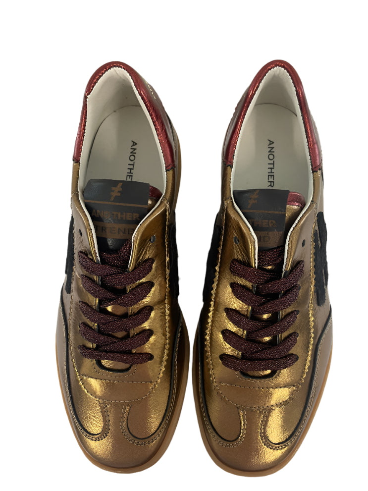 Pair of gold sneakers with brown laces on a white background