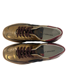 Load image into Gallery viewer, Gold sneakers with brown laces on a white floor next to a wooden object.
