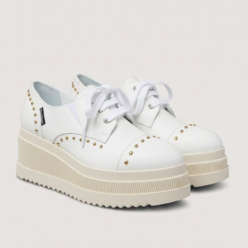 White platform sneakers with studded details on a light gray background
