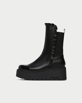 A black leather ankle boot with a chunky platform sole, featuring a ruffled elastic side panel and a small heel pull tab, shown from a side profile on a light gray background.