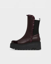 Load image into Gallery viewer, A dark burgundy leather ankle boot with a black elastic side panel, ruffled trim, and a chunky black platform sole, shown from a side profile on a light gray background.
