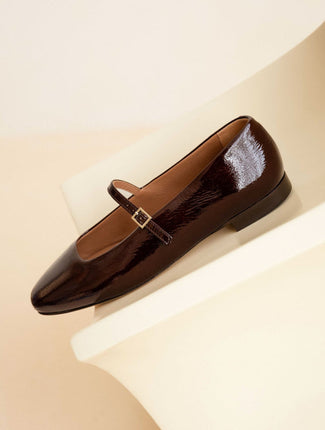 Shiny brown flat shoe with a strap on a beige background