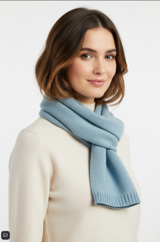 A woman with shoulder-length brown hair wearing a light blue knit scarf and a cream-colored sweater, photographed against a clean white background.