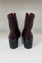 Load image into Gallery viewer, A pair of dark burgundy leather ankle boots with black block heels, shown from the back on a light gray surface.
