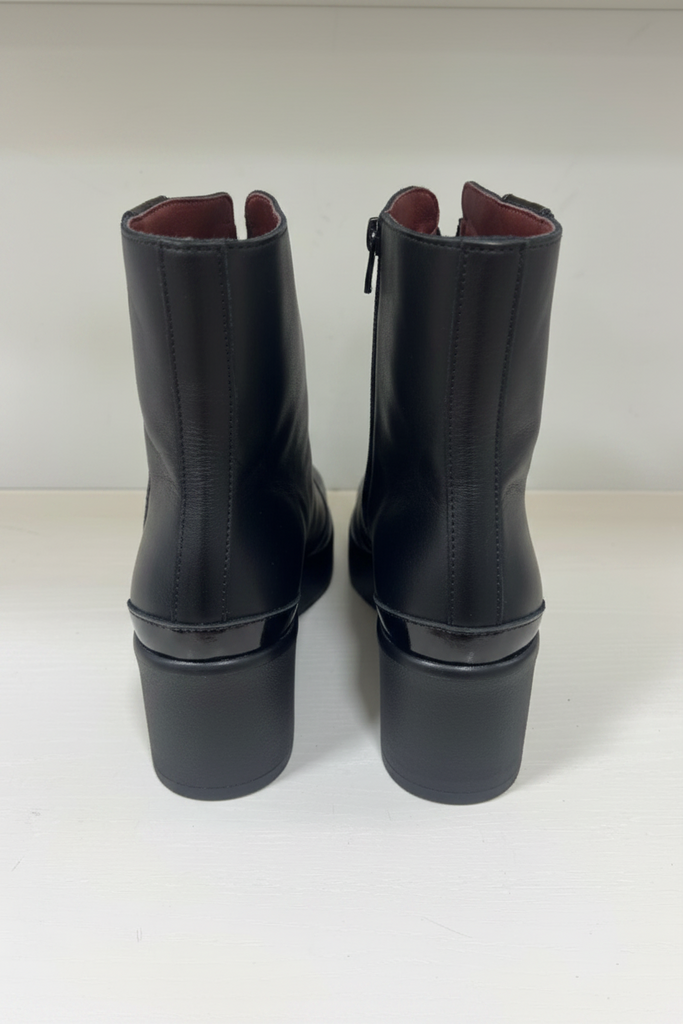 A pair of black leather ankle boots with block heels, shown from the back on a white surface against a white background.