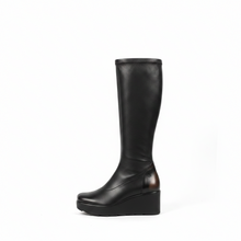 Load image into Gallery viewer, A pair of black knee-high leather boots with chunky platform wedge heels, shown from a side profile against a plain light gray wall and white floor.
