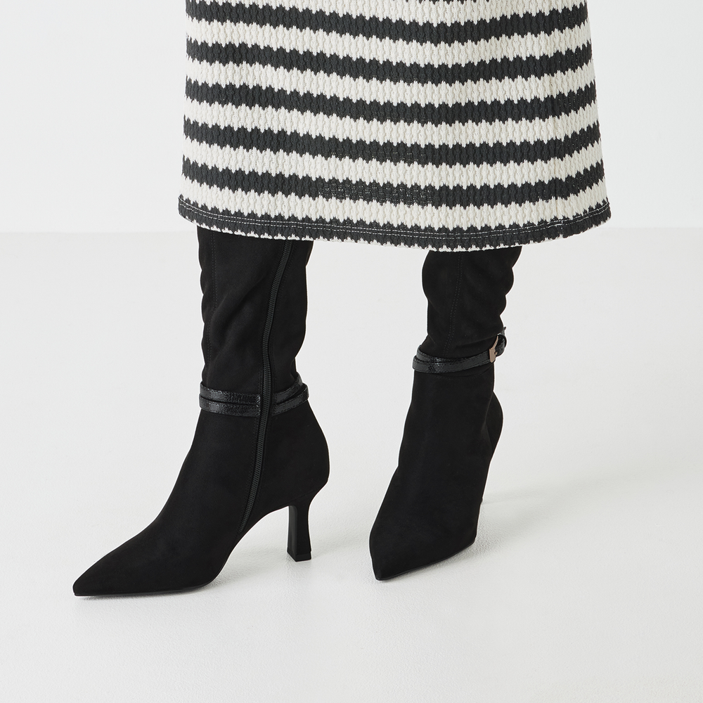 Black high-heeled boots worn with a striped coat on a white background