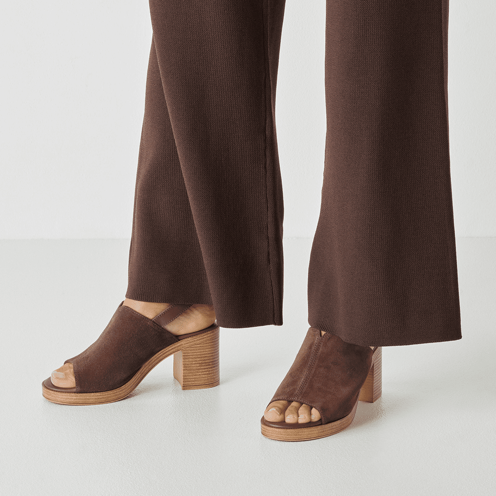 Brown suede sandals worn with brown pants on a light gray background