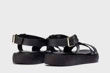 Load image into Gallery viewer, Black sandals with gold buckles on a light gray background
