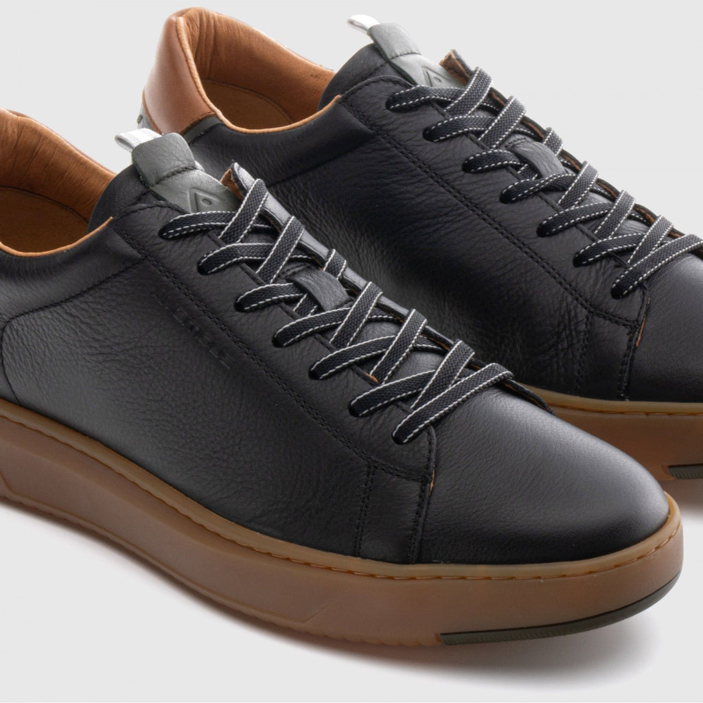 Black leather sneakers with brown soles on a light gray background