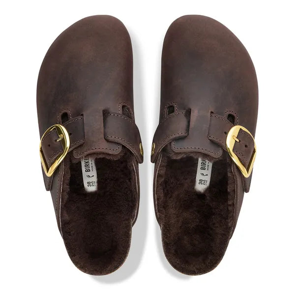 A pair of dark brown Birkenstock clogs with a plush brown faux fur lining and gold-tone buckle straps, shown from a top-down view on a white background.