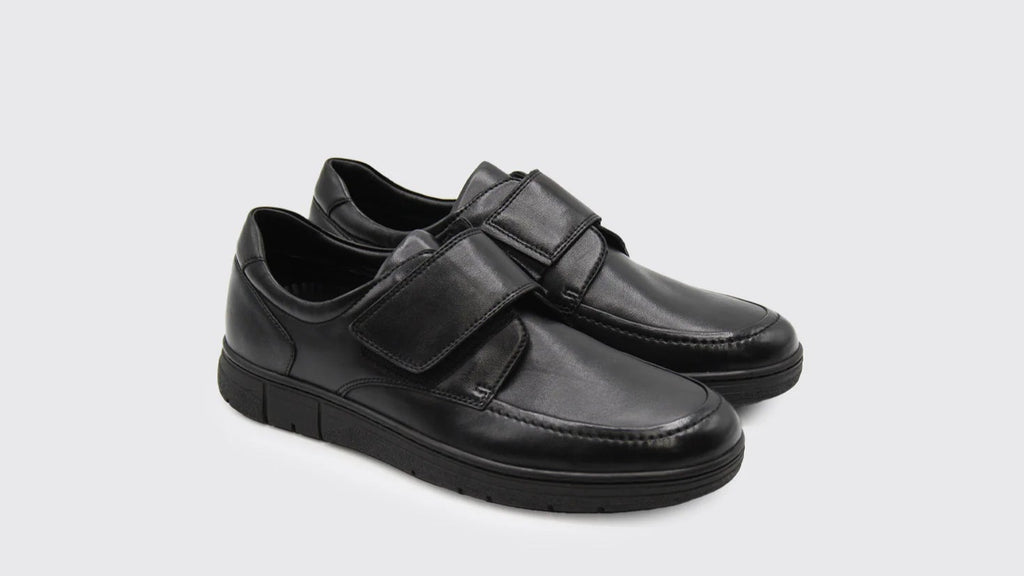 Black leather shoes with velcro straps on a light gray background