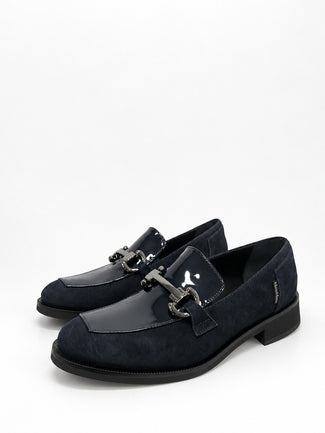 A pair of dark navy blue loafers with a mix of suede and patent leather panels, featuring a decorative silver-tone horsebit detail across the vamp, set against a plain white background.