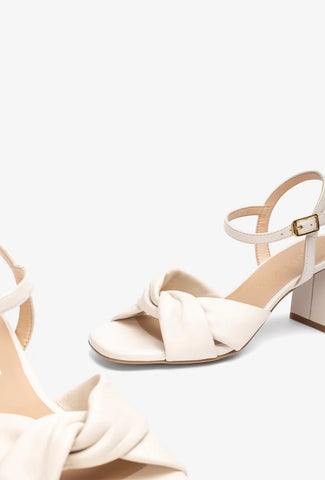 Person wearing a black dress with a high slit and beige sandals on a white background