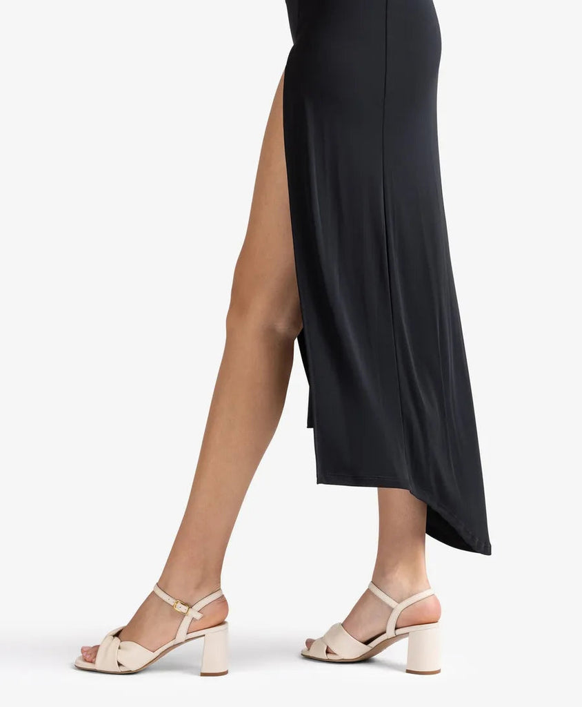 Person wearing a black dress with a high slit and beige sandals on a white background