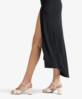 Person wearing a black dress with a high slit and beige sandals on a white background