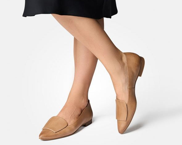 Tan loafers worn with a black skirt on a white background