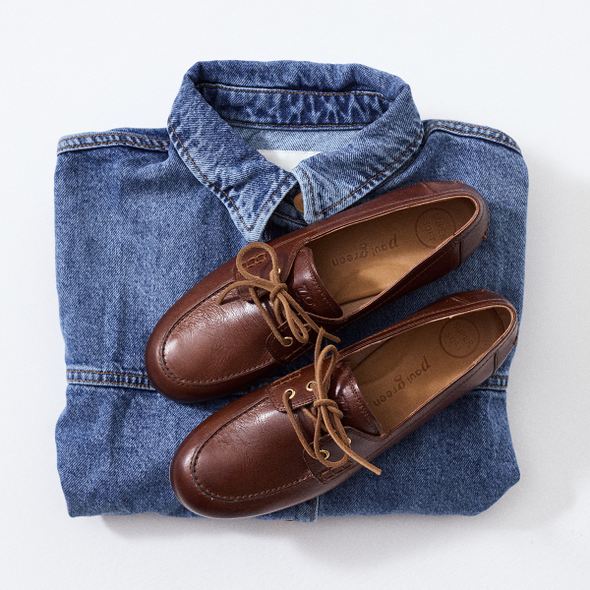 Brown loafers on a folded denim shirt with a white background