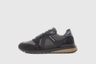 Black sneaker with brown sole on a light gray background